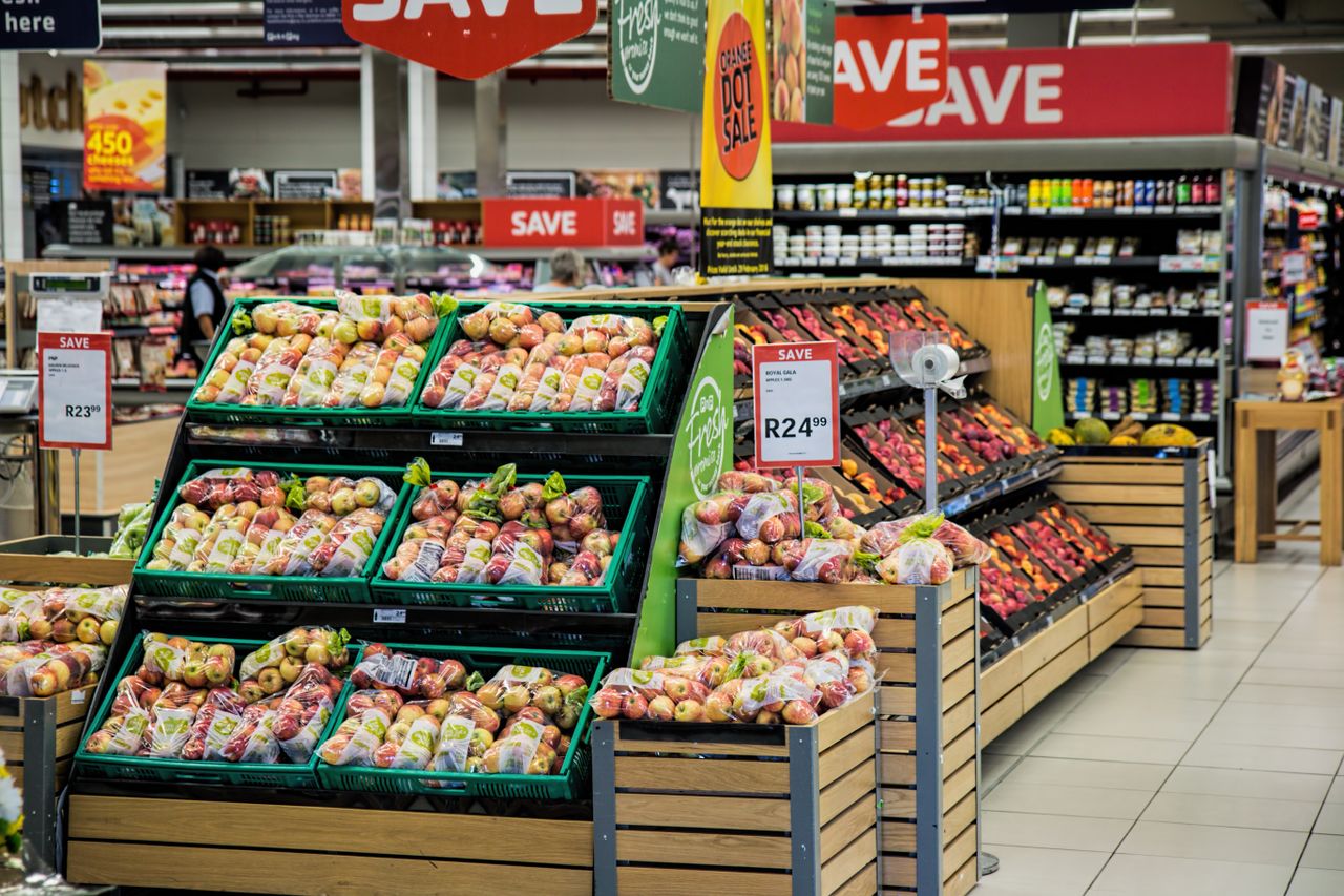 A grocery cart in a supermarket aisle with fresh food, representing lower grocery prices