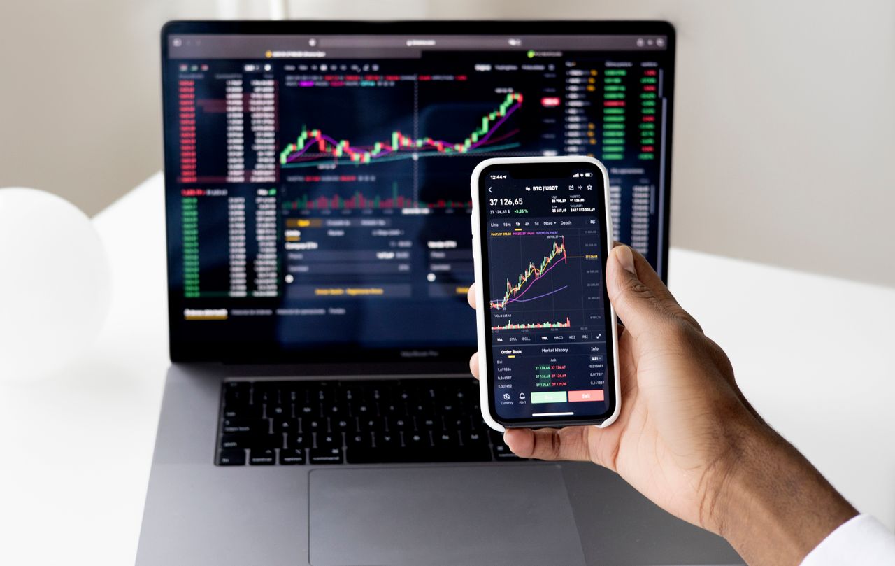 A laptop showing market charts beside a notebook, representing active and passive investing strategies