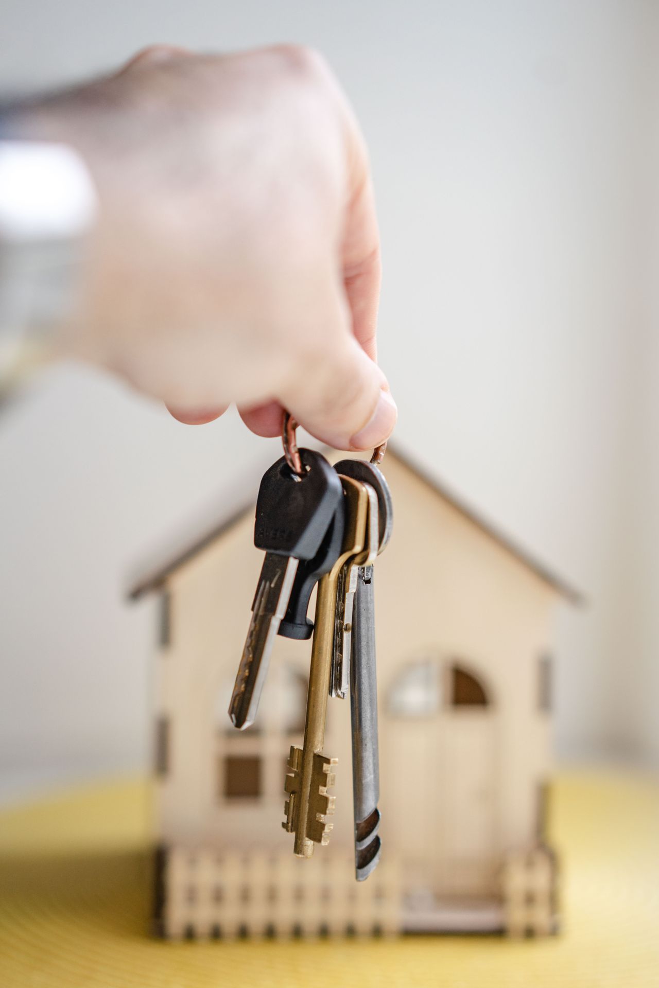 Hand holding keys beside a model house, the decision point before getting a mortgage